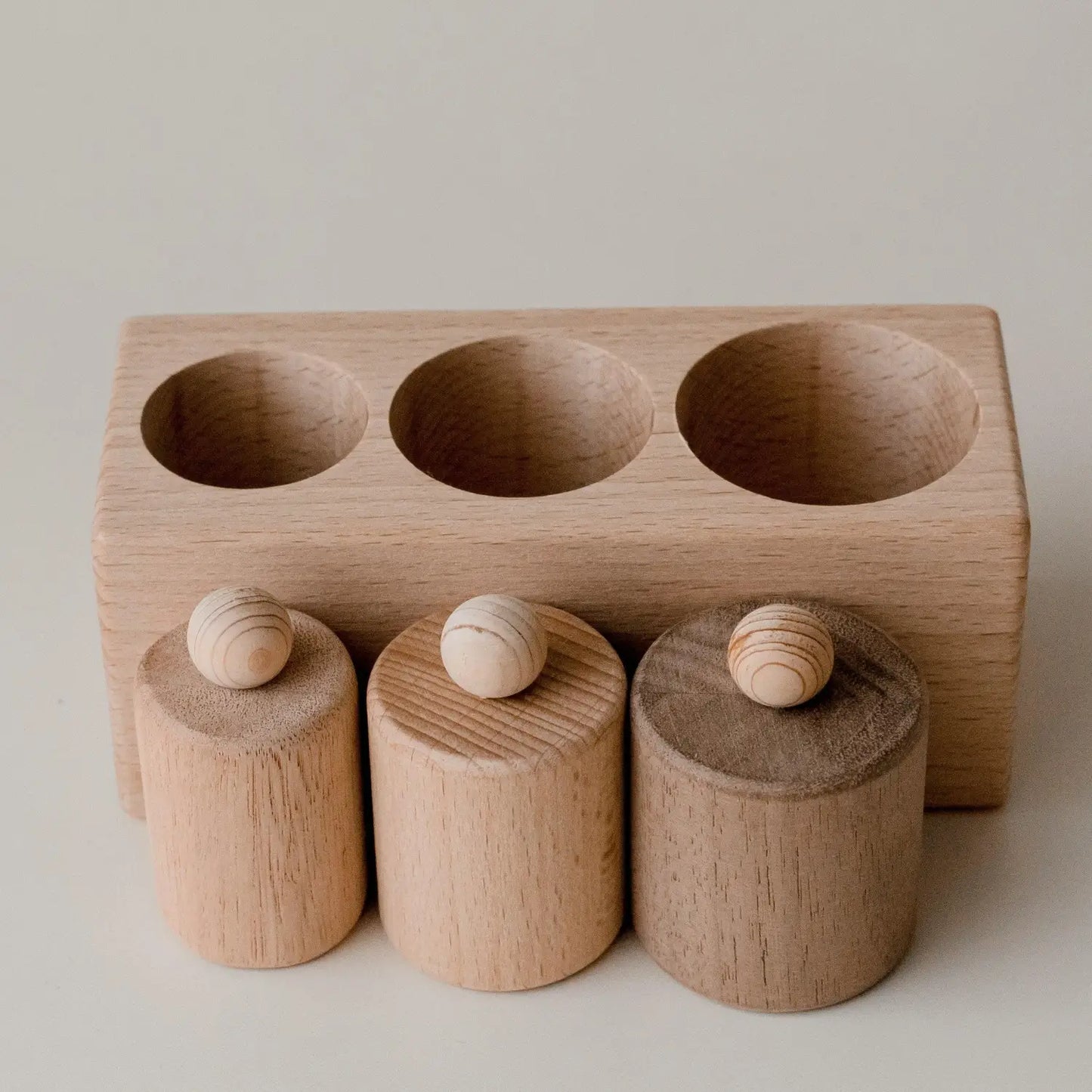 Wooden toy or educational tool with three cylindrical pieces fitting into corresponding holes.
