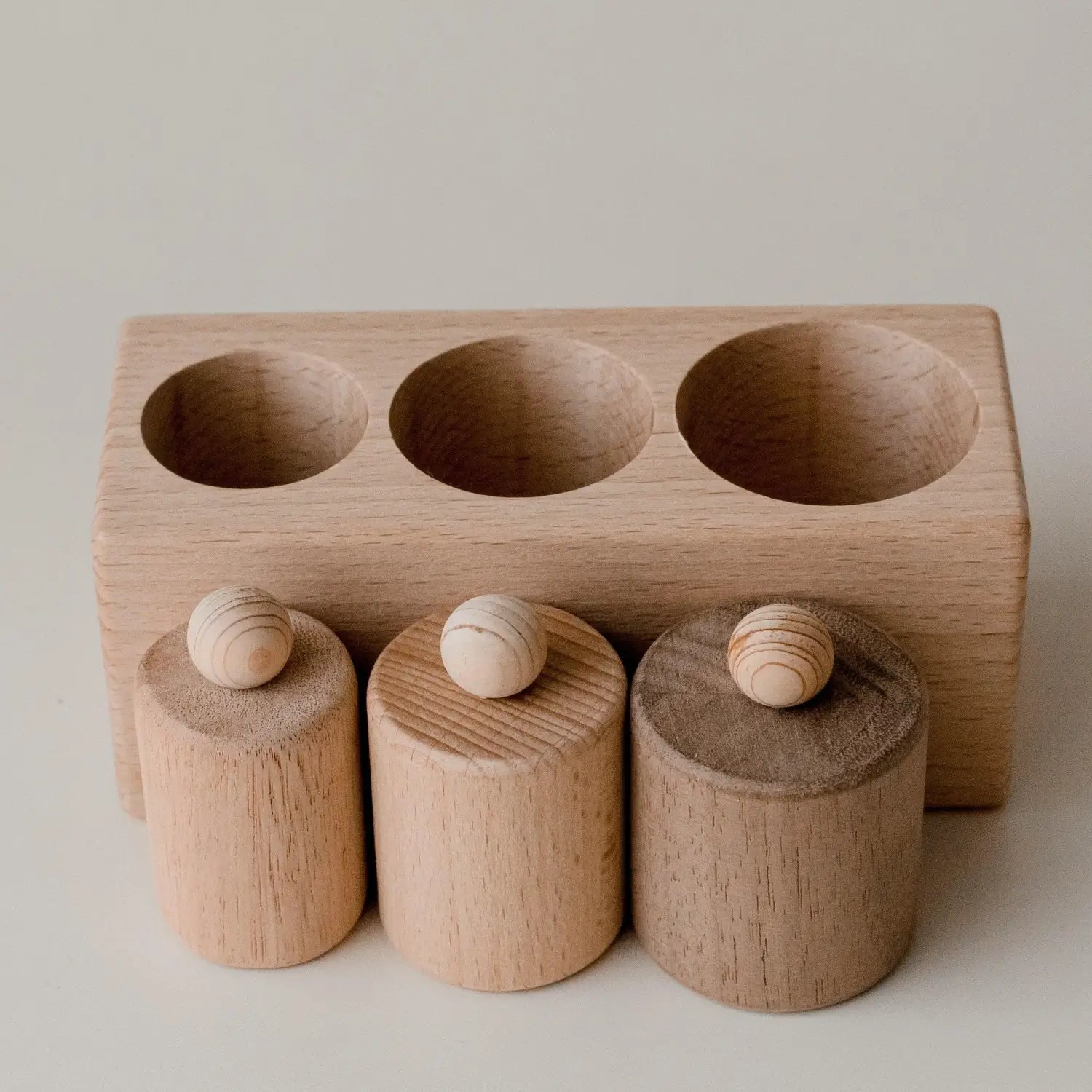 Wooden toy or educational tool with three cylindrical pieces fitting into corresponding holes.
