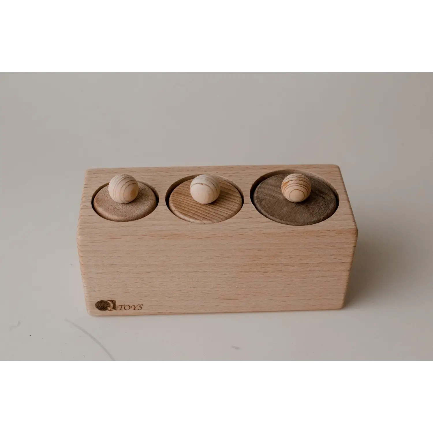 Wooden block with three circular indentations and matching spherical knobs.