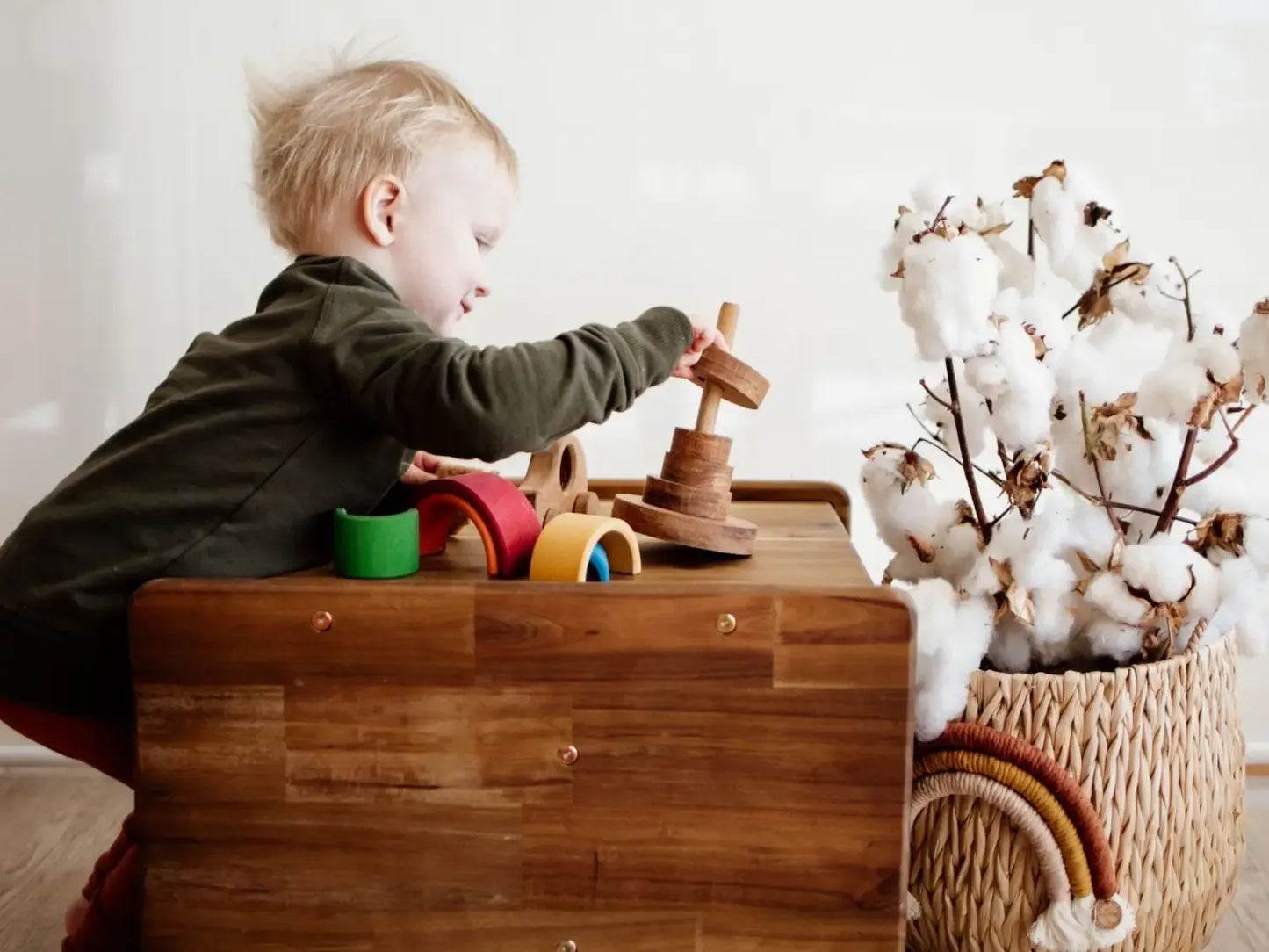 Young child playing with wooden toys on a wooden chest.