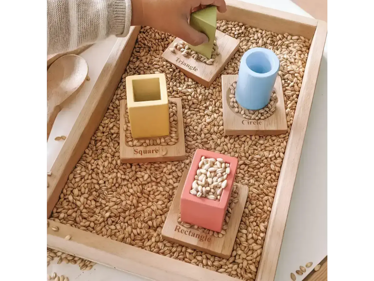 Wooden tray filled with grain and colorful geometric blocks for sensory play or learning activities.
