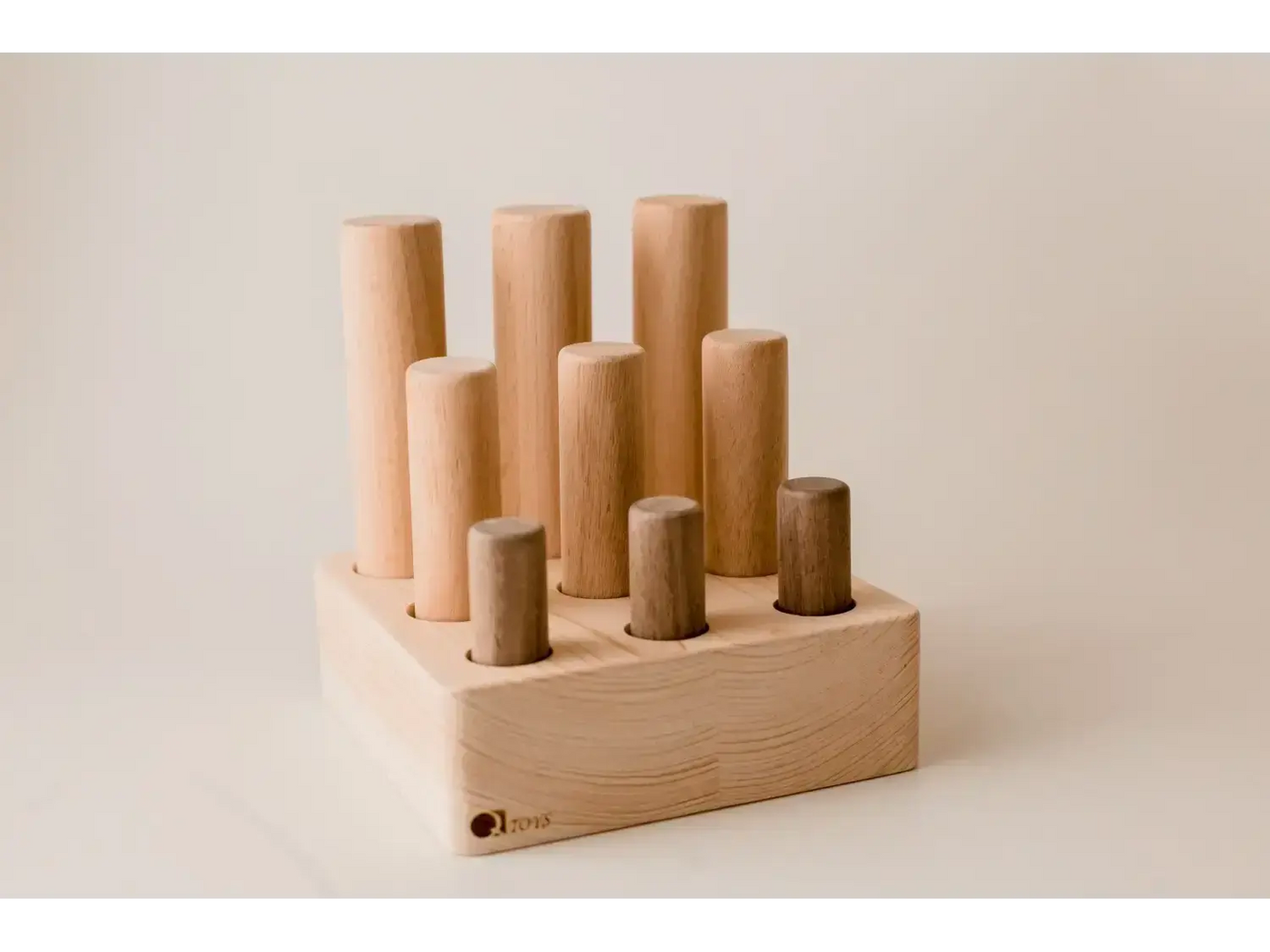Wooden block with cylindrical pegs of varying heights inserted into holes.