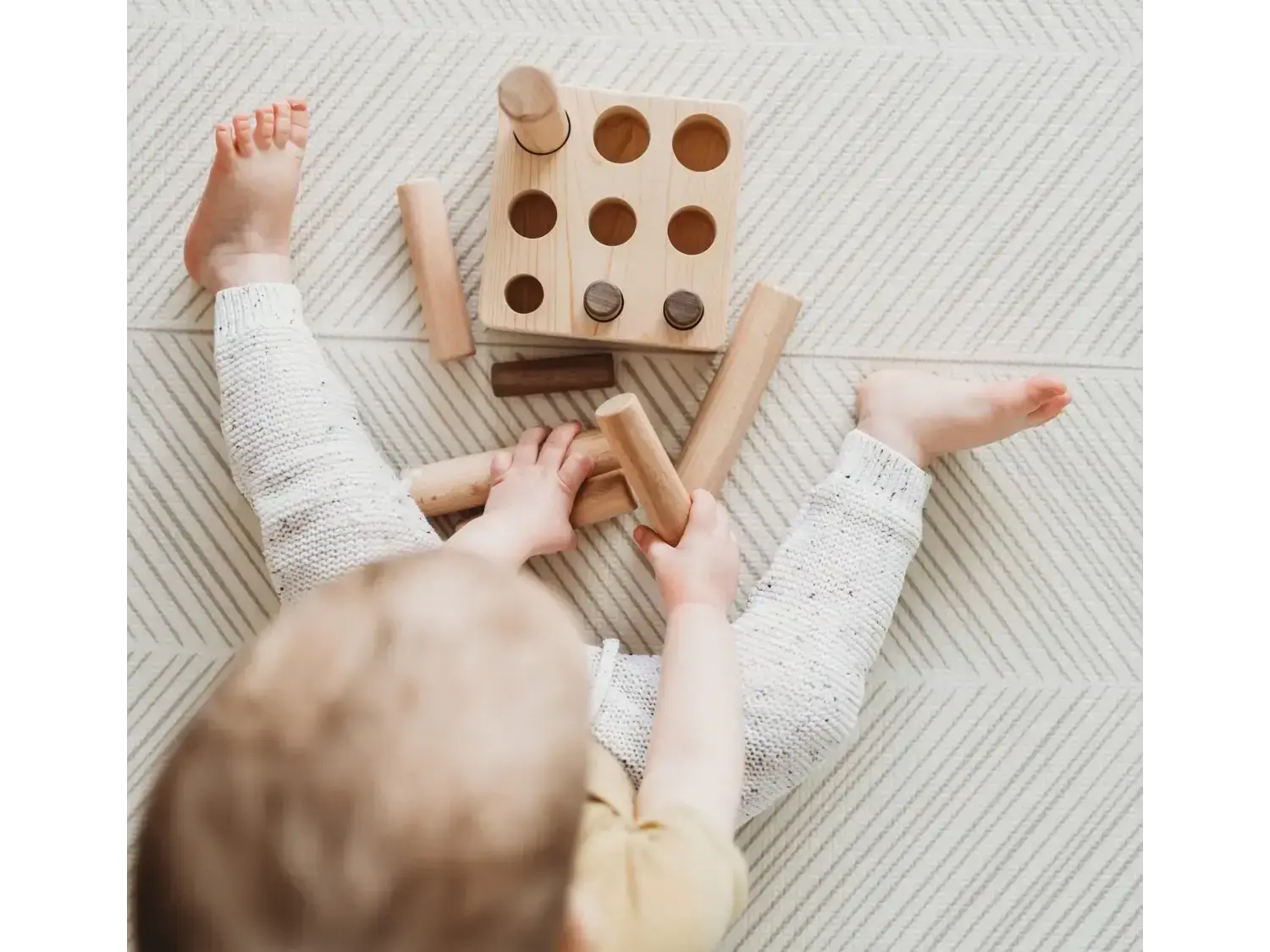 Wooden toy with circular holes and pegs for shape sorting.
