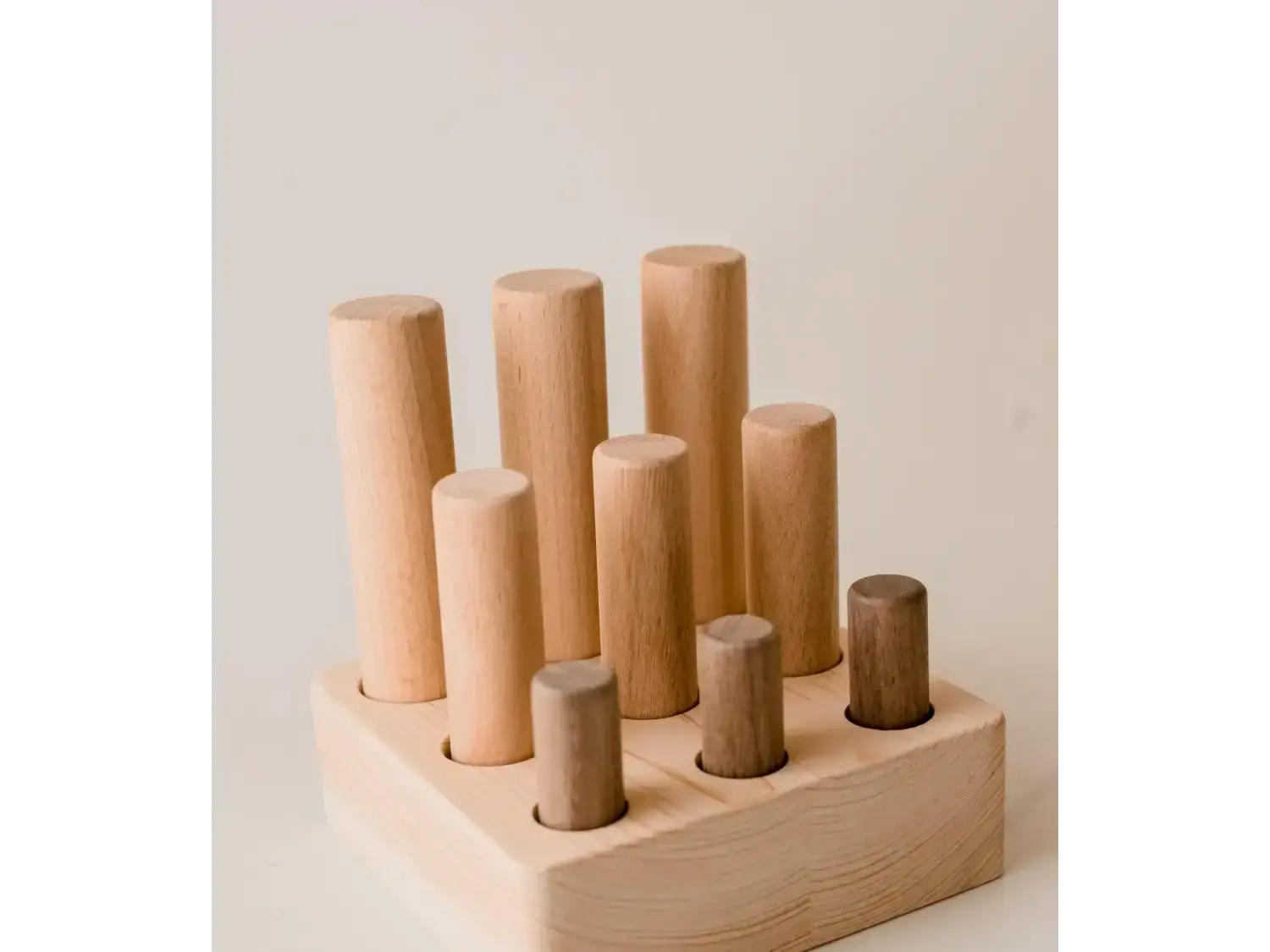 Wooden toy with cylindrical pegs of varying heights inserted into a base.
