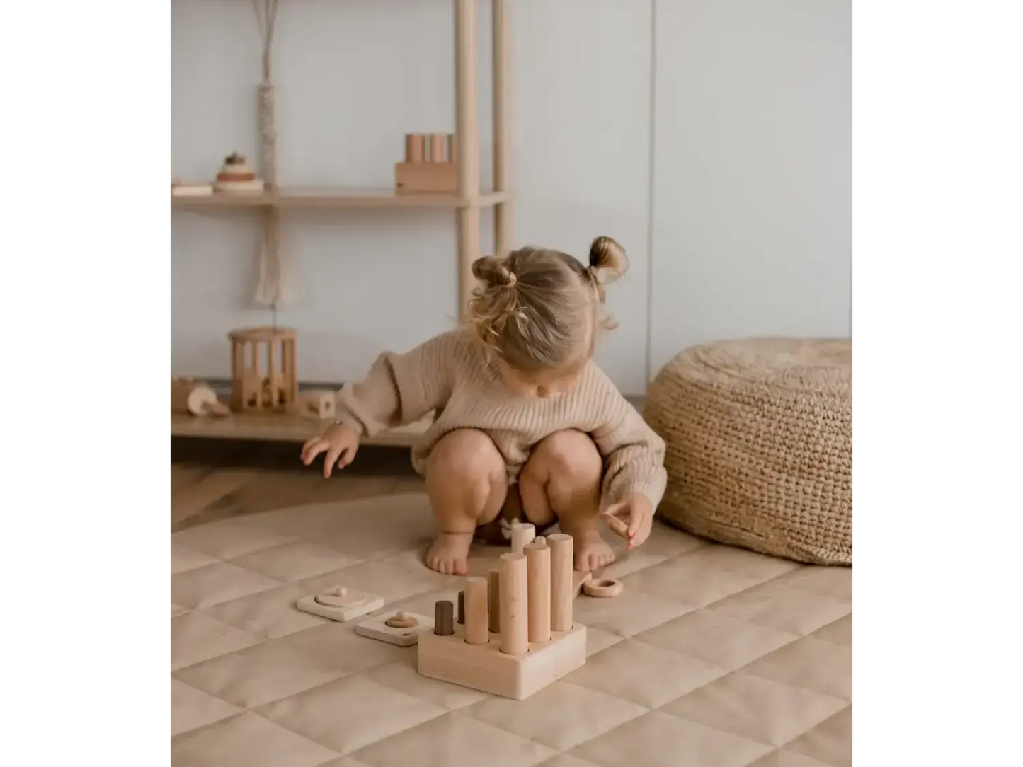 Toddler with hair buns playing with wooden blocks on a circular mat.