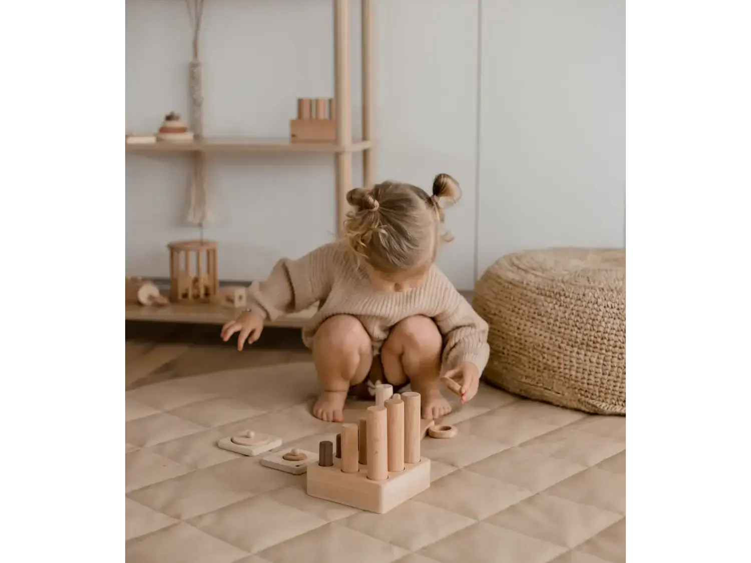 Toddler with hair buns playing with wooden blocks on a circular mat.