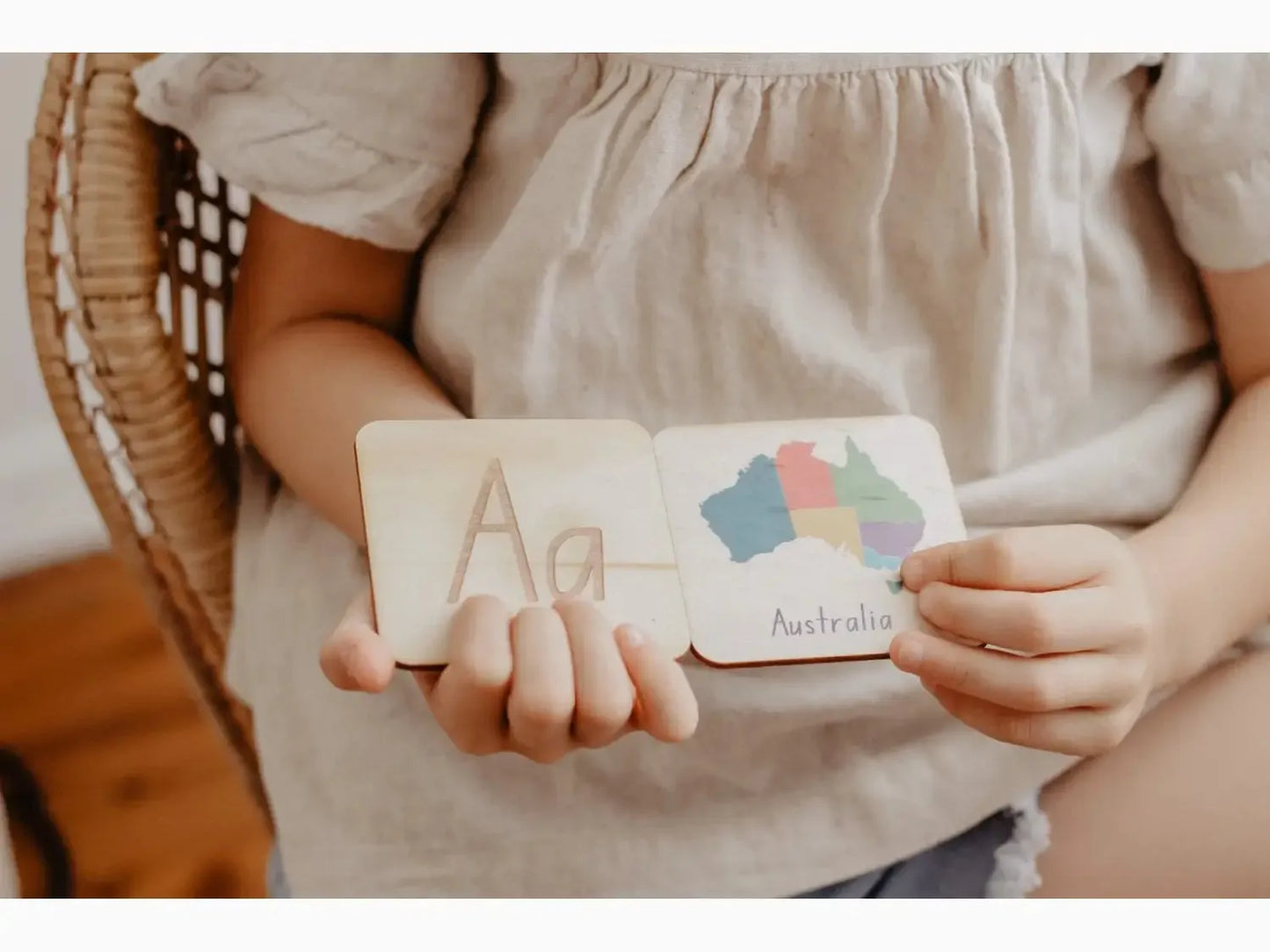 Wooden educational card or block with the letter ’A’ and colorful cloud shapes held by small hands.