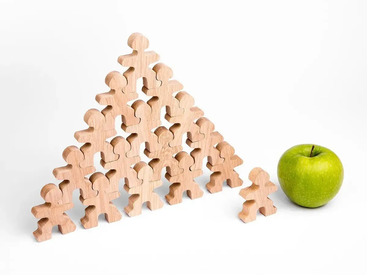Triangular stack of wooden human-shaped figures with one figure separate and a green apple beside it.