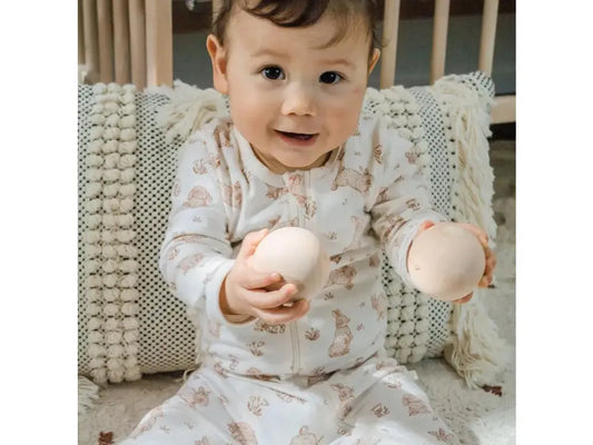 Baby in a patterned onesie holding two round objects.