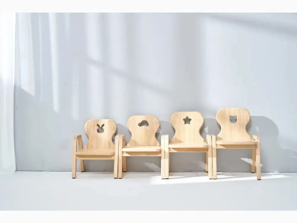 Four wooden children’s chairs with different cutout shapes in their backrests.
