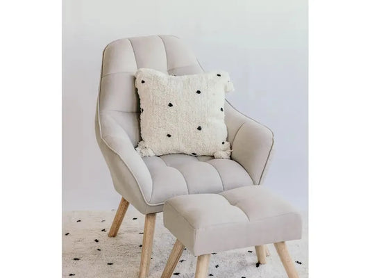 Beige upholstered armchair with matching footstool and decorative pillow.