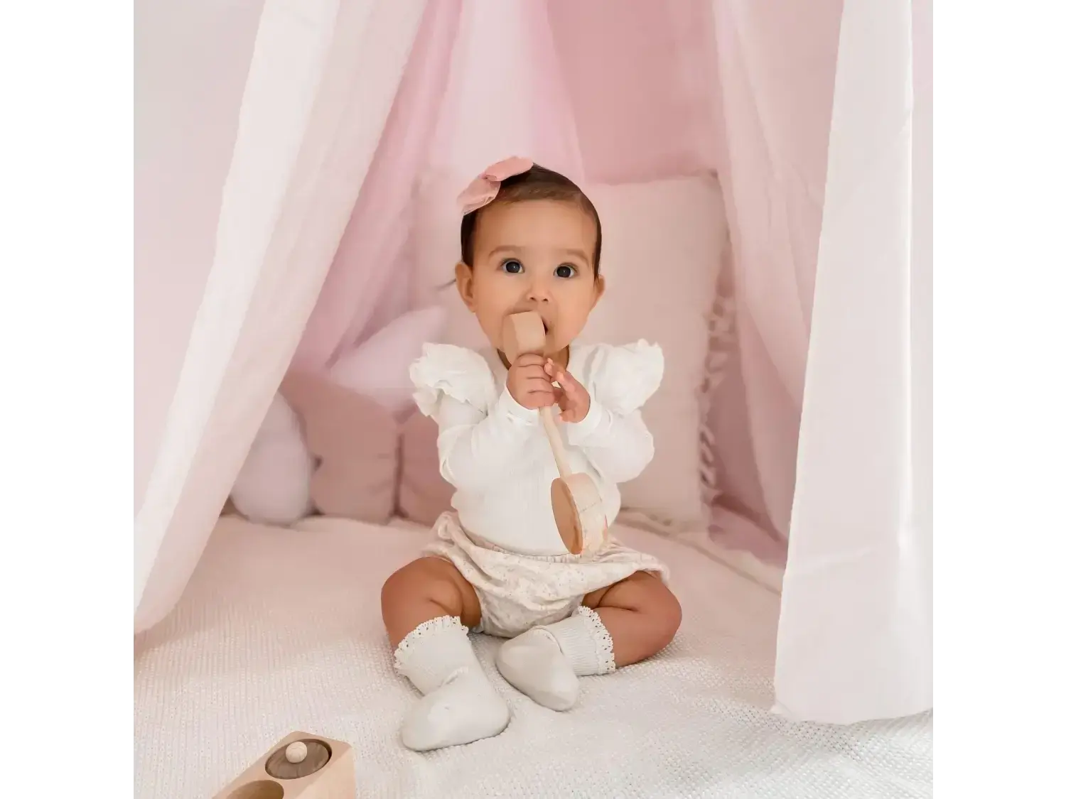 Baby wearing a white outfit sitting on a soft surface.