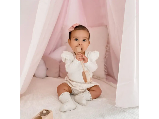 Baby wearing a white outfit sitting on a soft surface.