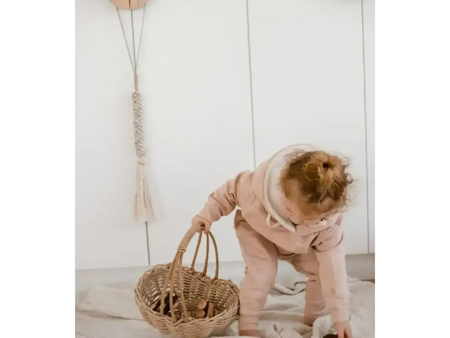 Toddler in a pink outfit bending over to reach into a woven basket.