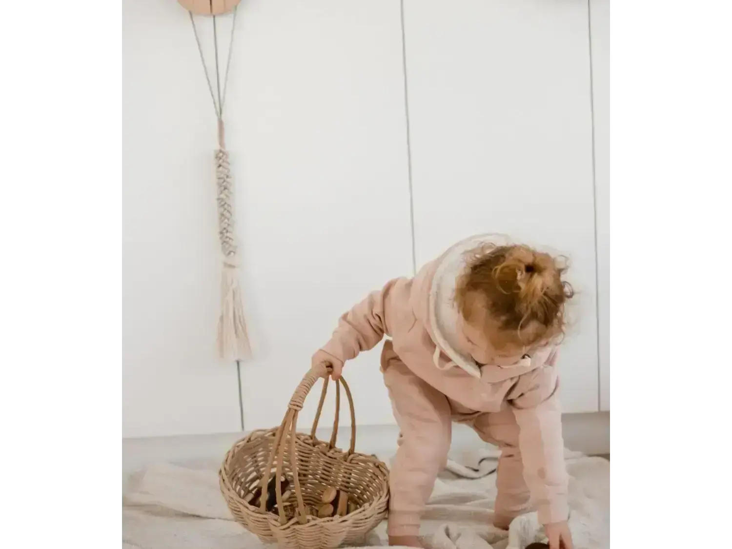 Toddler in a pink outfit bending over to reach into a woven basket.