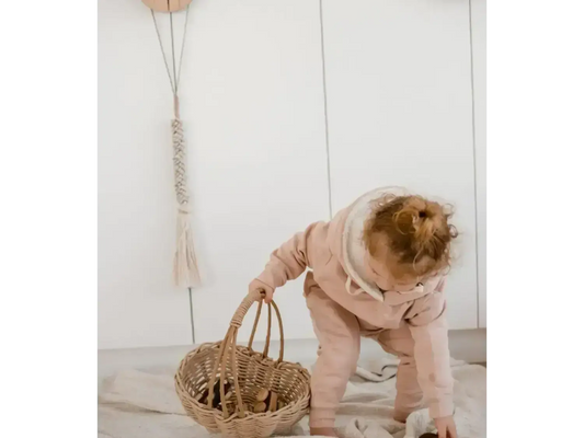 Toddler in a pink outfit bending over to reach into a woven basket.