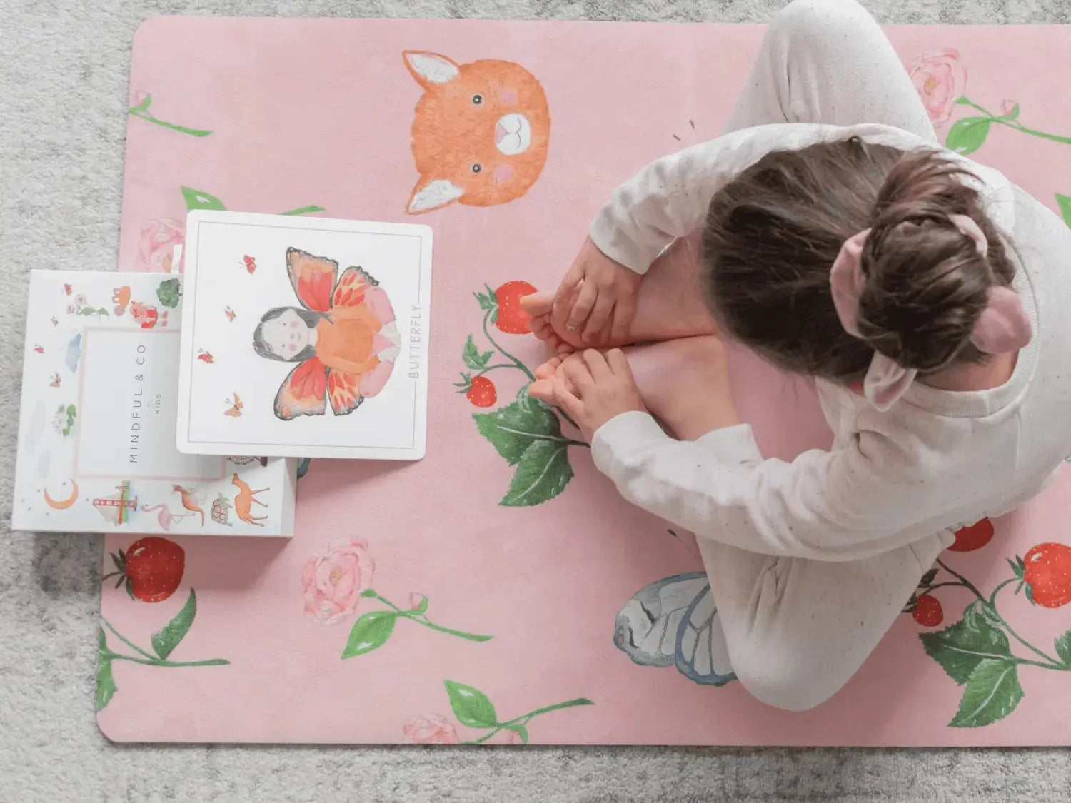 Child sitting on a pink floral rug with illustrated cards.