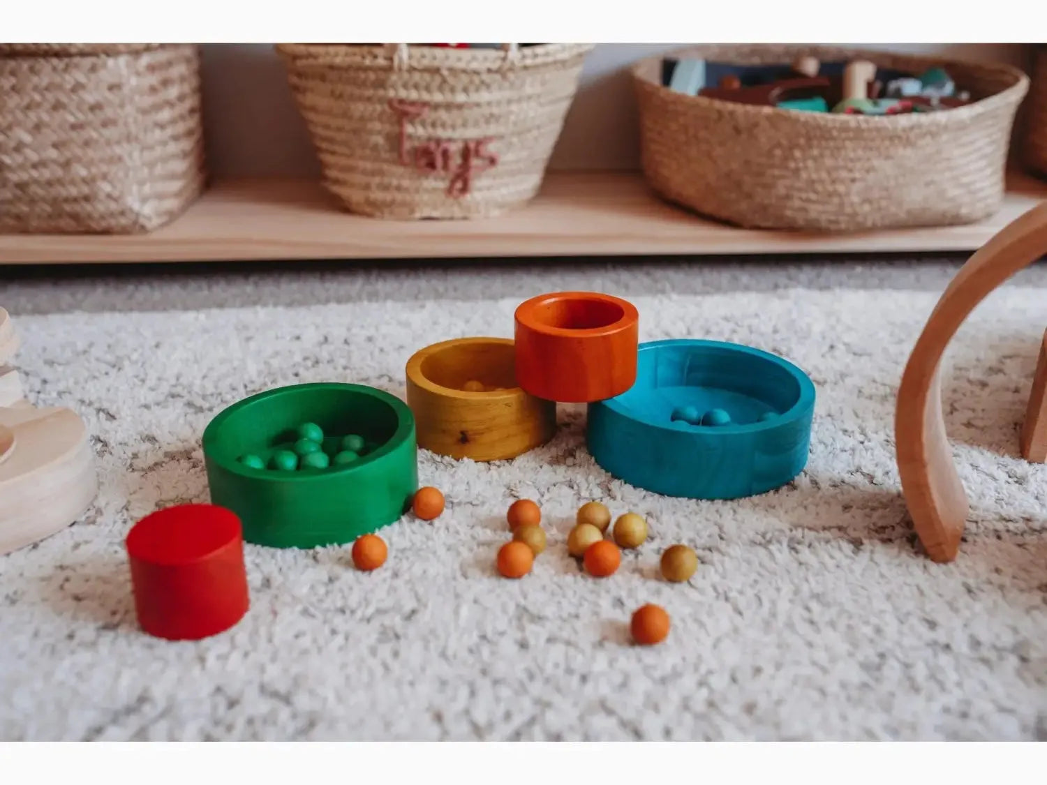 Colorful stacking rings toy with small wooden balls scattered around it.