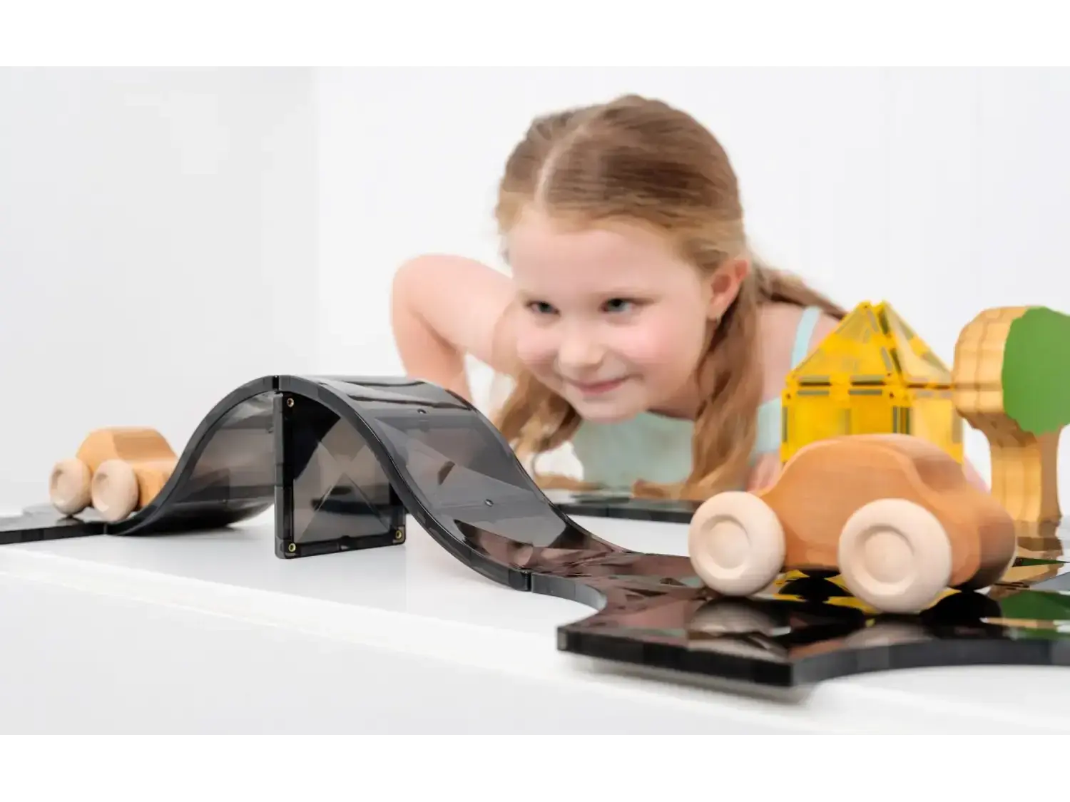 Young child playing with wooden toy vehicles and a toy road or track.