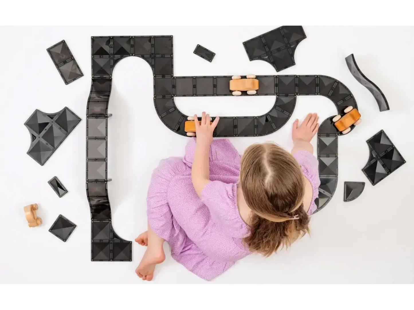 Child in a purple shirt playing with a toy car track on a white surface.