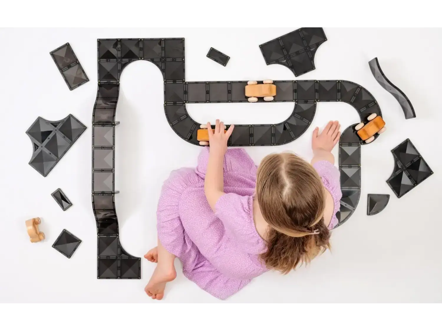 Child in a purple shirt playing with a toy car track on a white surface.