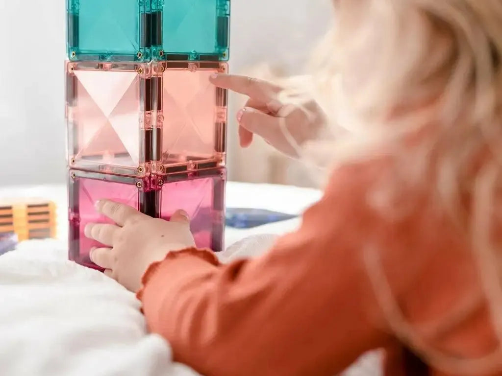 Colorful stacked magnetic building tiles being played with by small hands.