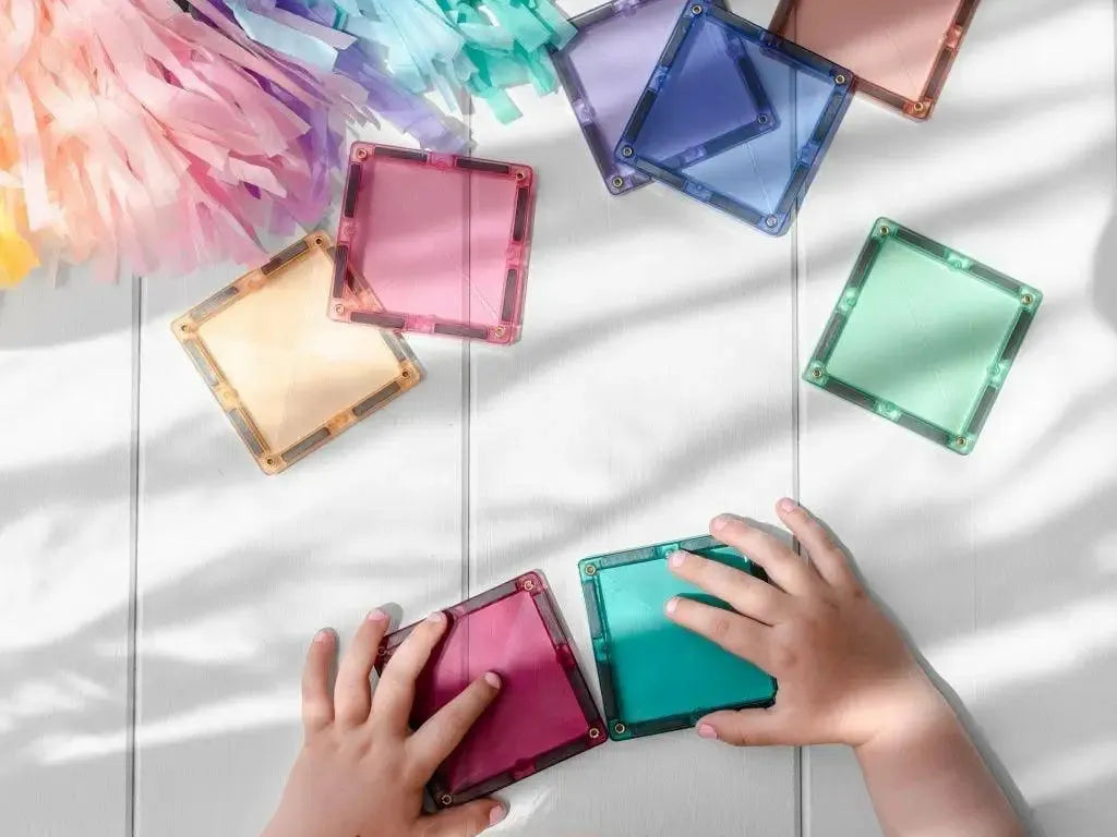 Colorful square magnetic tiles being arranged by a child’s hands.