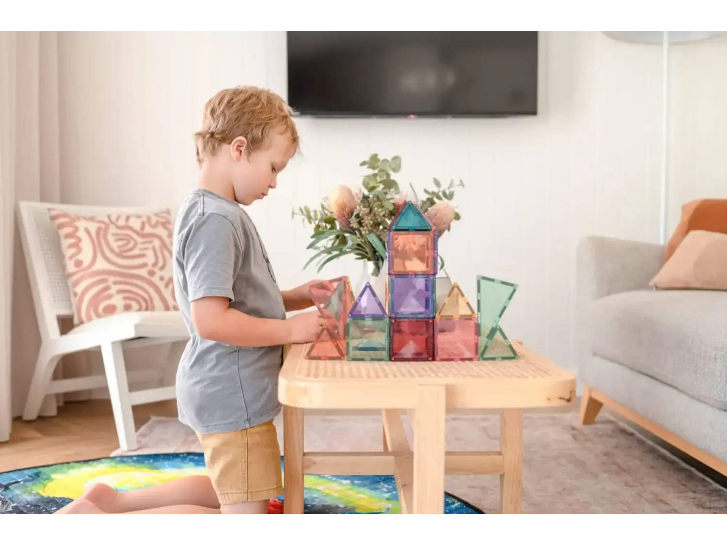 Child playing with colorful magnetic building tiles on a wooden table.