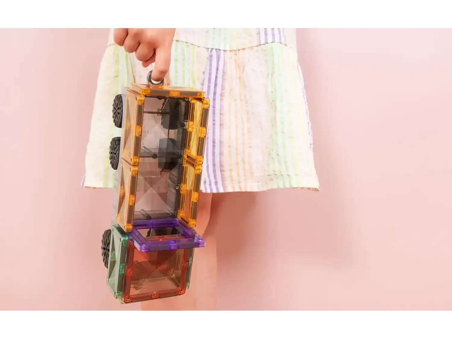 Colorful magnetic building tiles held by a hand against a pastel background.