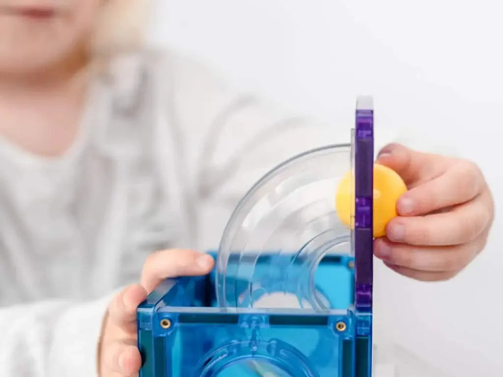Blue transparent plastic device with tubes and a yellow ball, likely an educational science toy or experiment kit.
