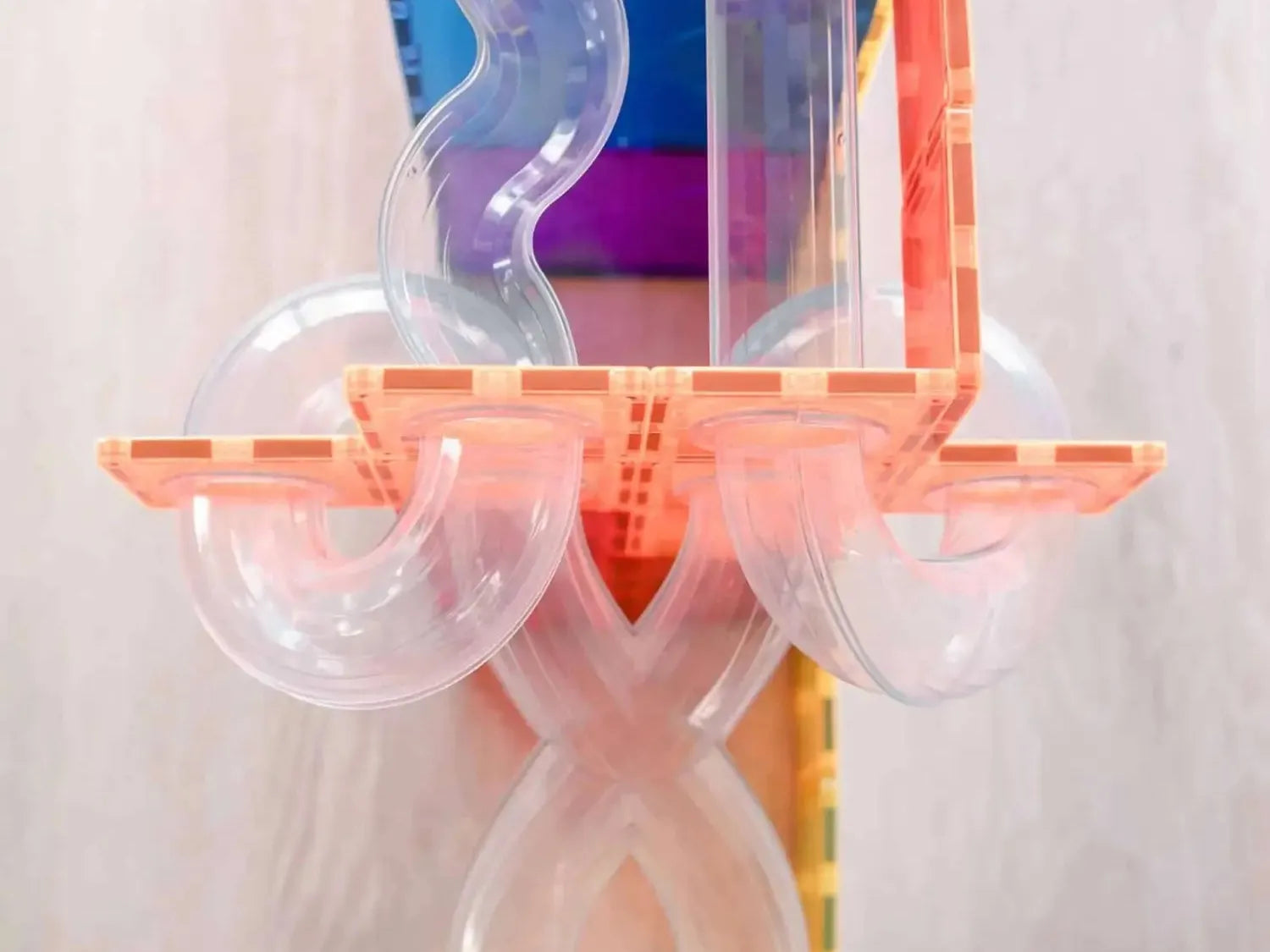 Transparent plastic or glass sculpture with curved and straight tubular shapes connected to a central X-like structure.