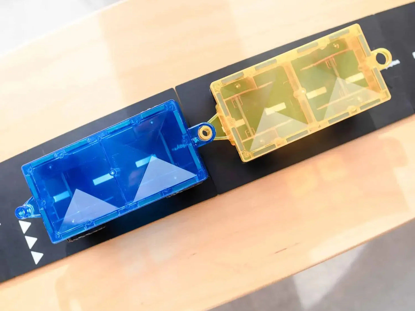 Two translucent plastic containers, one blue and one yellow, attached to a black strip.
