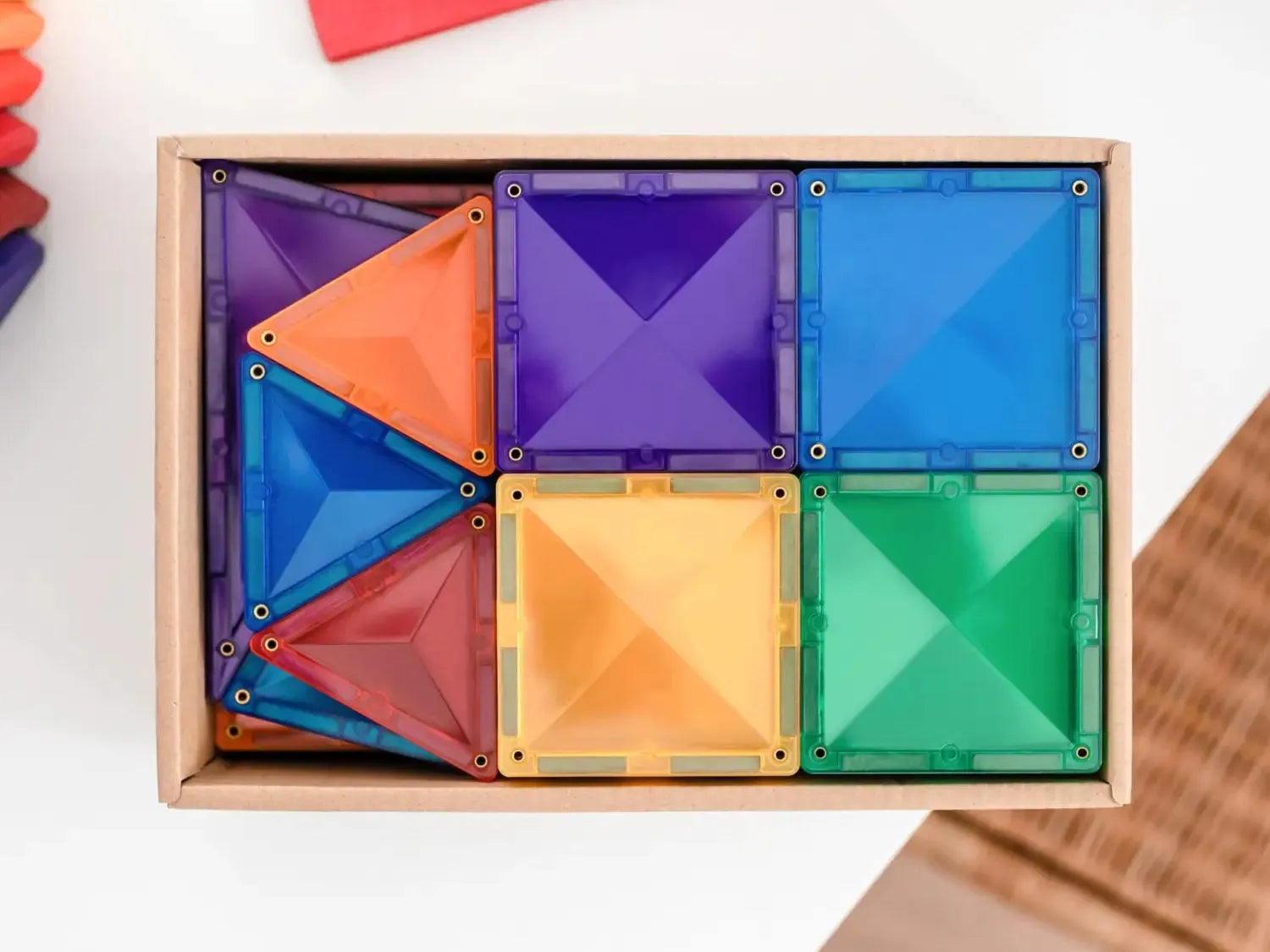 Wooden box containing colorful geometric magnetic tiles in various shapes and sizes.
