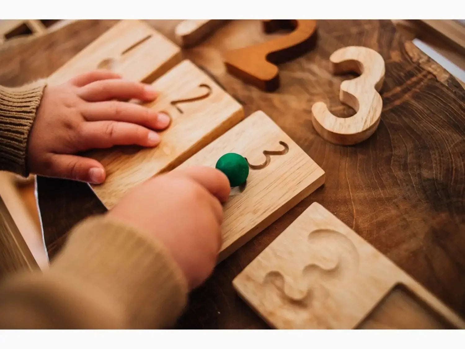 Wooden number puzzle pieces with small hands interacting with them.