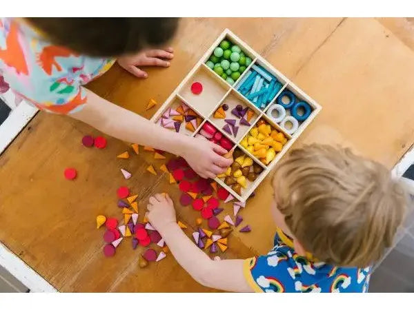 Wooden compartment tray filled with colorful craft materials and small objects.