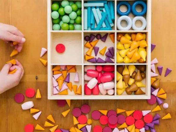 Wooden compartment box filled with colorful geometric shapes and objects.