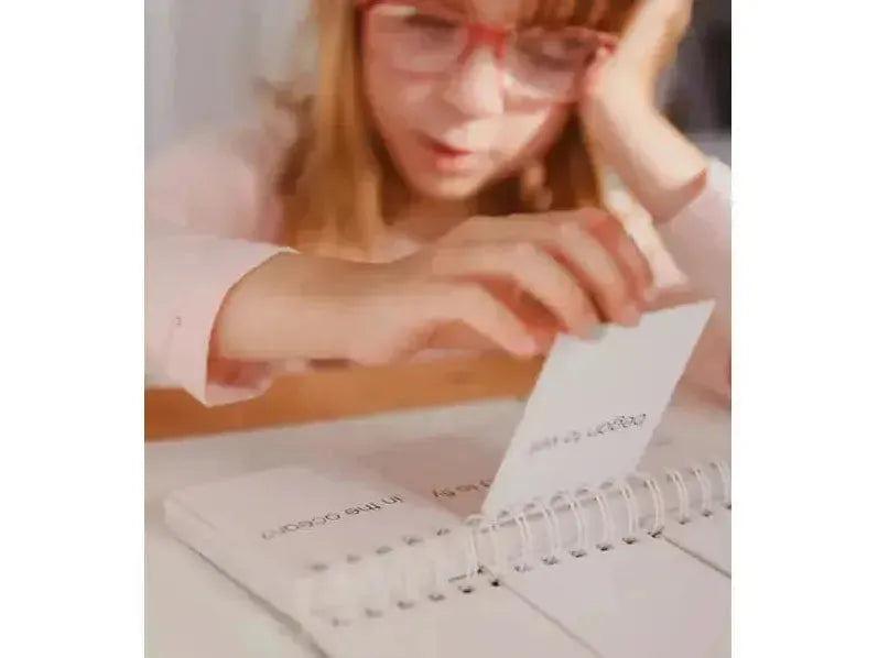 Person wearing red glasses writing in a spiral-bound notebook.