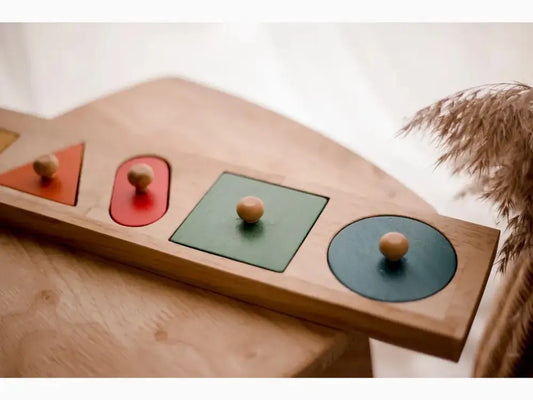 Wooden puzzle board with geometric shapes and knobs for grasping.