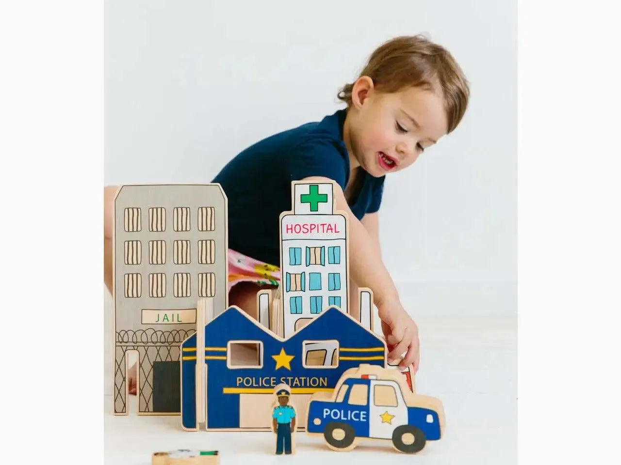 Wooden toy city playset featuring buildings and vehicles, including a police station and hospital.