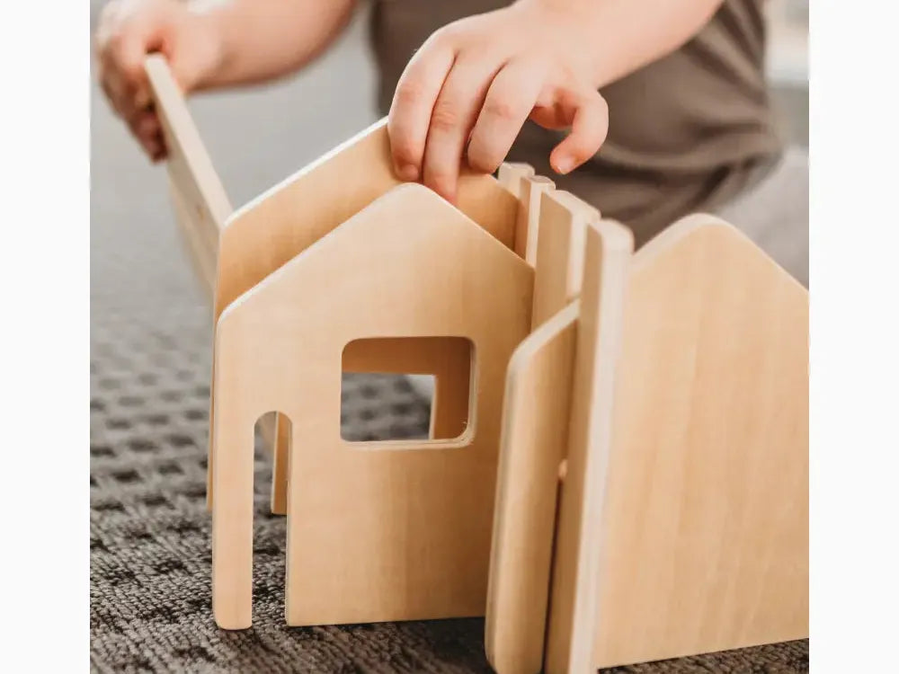 Wooden toy house with interlocking pieces being assembled by hands.