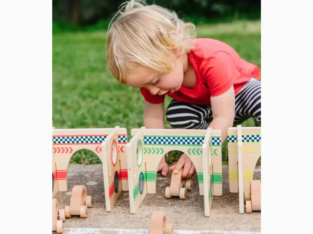 Child playing with a wooden toy race track or bridge structure on the ground.