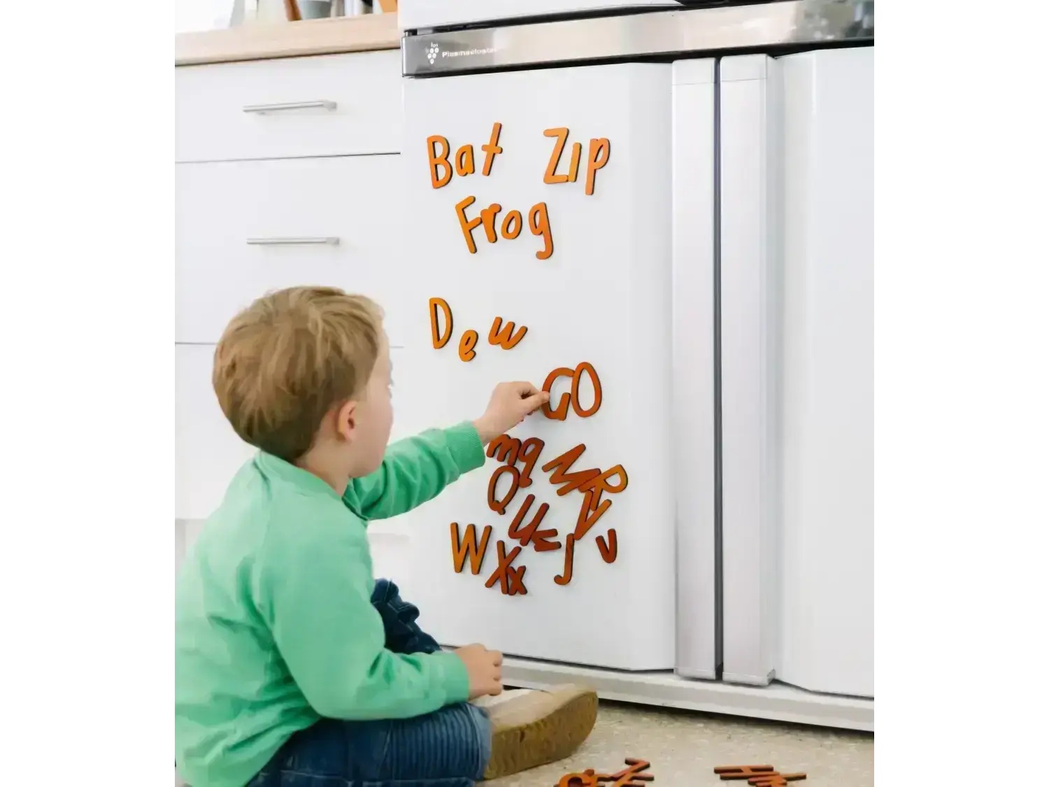 Child playing with magnetic letters on a refrigerator door.