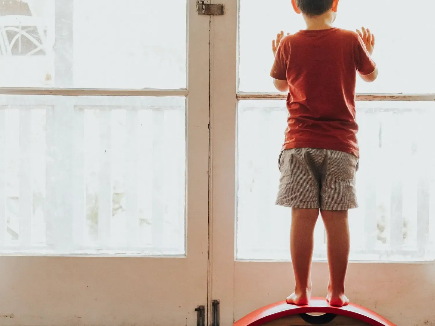 Child standing on a balance board in front of a glass door.