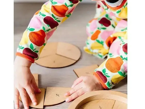 Colorful fruit-patterned long-sleeved shirt worn by someone manipulating wooden puzzle pieces.