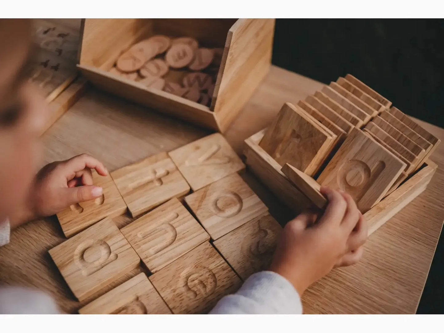 Wooden number blocks or tiles with carved numerals being handled by small hands.