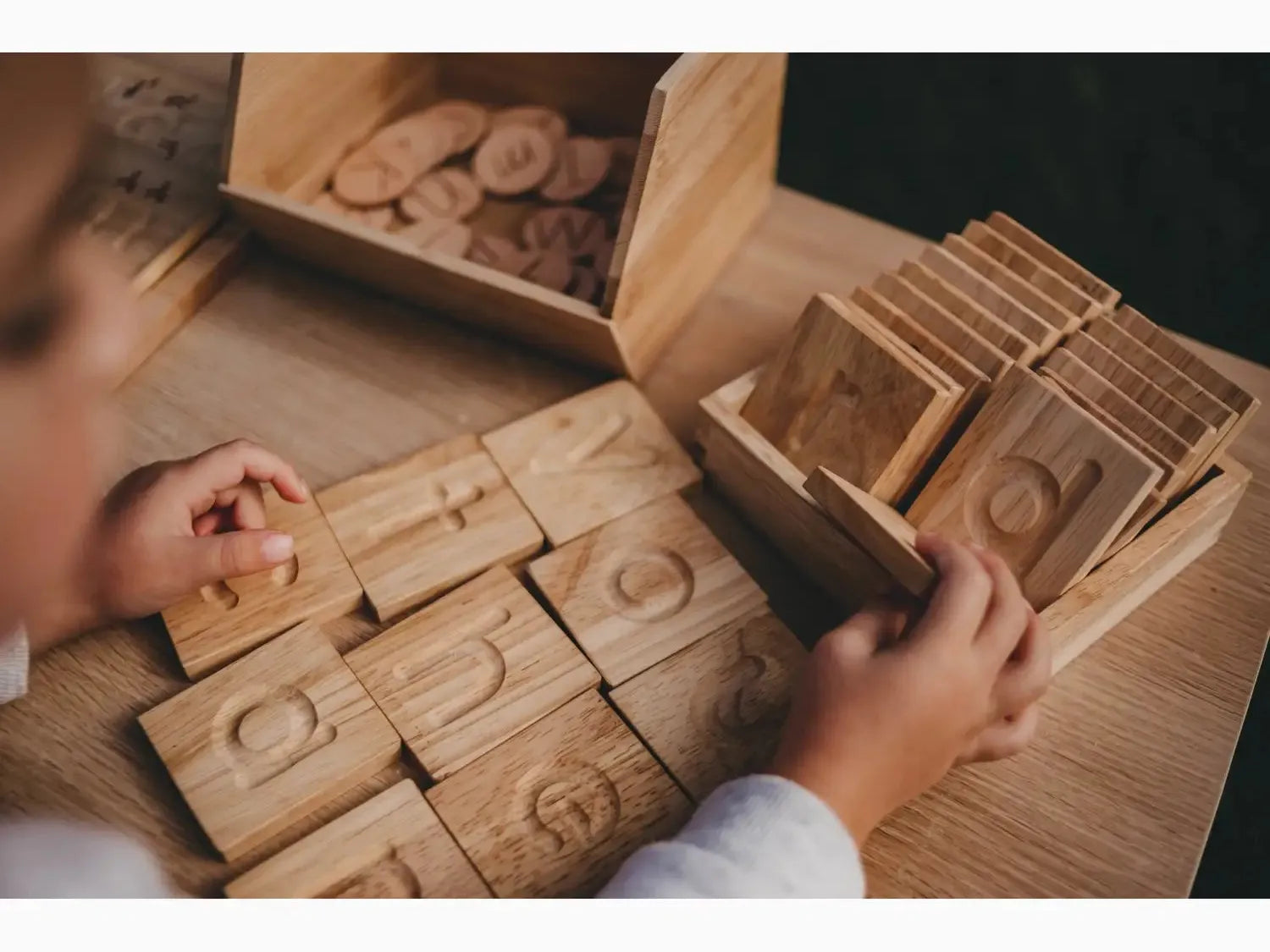 Wooden number blocks or tiles with carved numerals being handled by small hands.