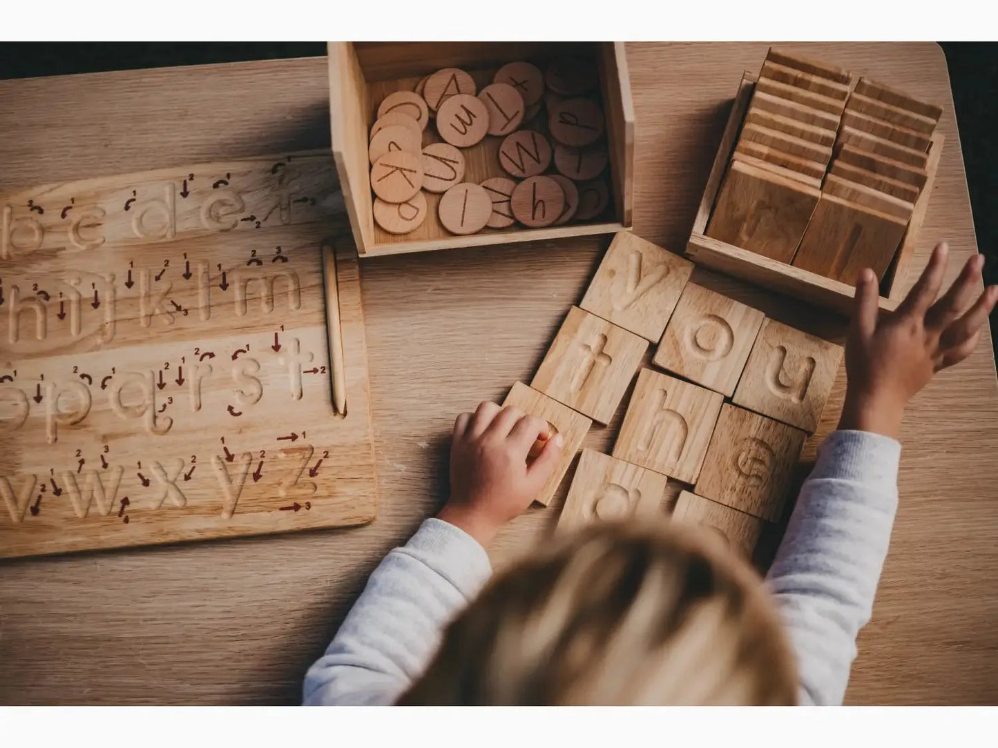 Wooden alphabet blocks and letter tiles being arranged by small hands on a table.