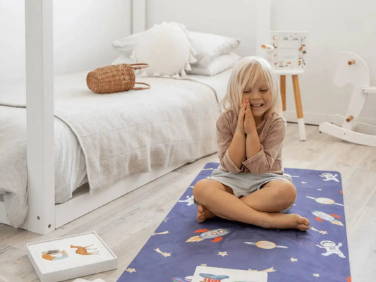 Child sitting cross-legged on a patterned play mat in a bedroom.