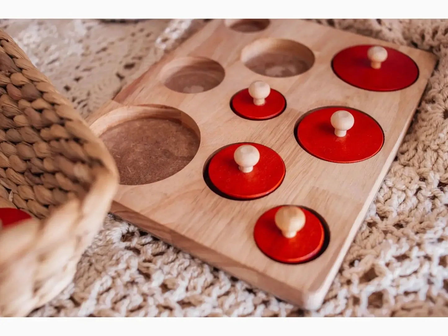 Wooden board with circular indentations and red discs containing small knobs.