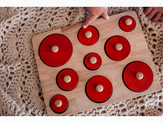 Wooden puzzle board with red circular pieces of varying sizes.